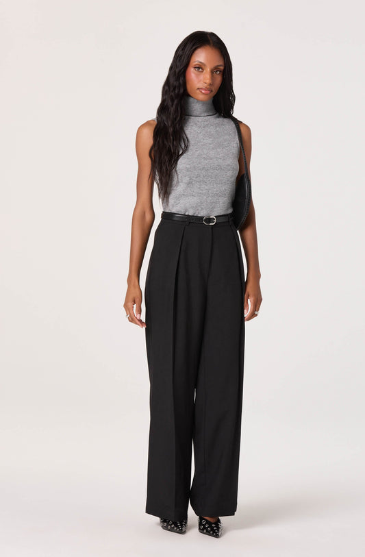 A woman is wearing a sleeveless, high-neck gray top made of a soft, knit fabric. She pairs it with high-waisted black wide-leg trousers that have a belt with a round buckle. She completes her outfit with black high-heeled shoes featuring a patterned design.
