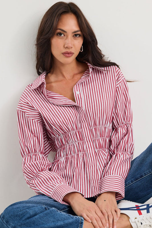 Woman wearing a red and white striped shirt and blue jeans sitting on a white floor.
